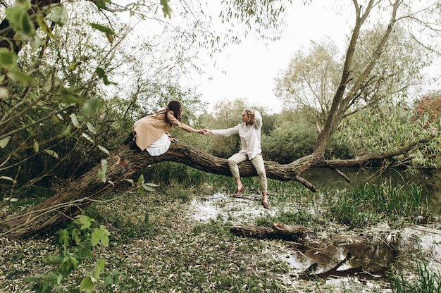 Un beau couple dans le style boo embrasse assis sur une branche au-dessus du lac