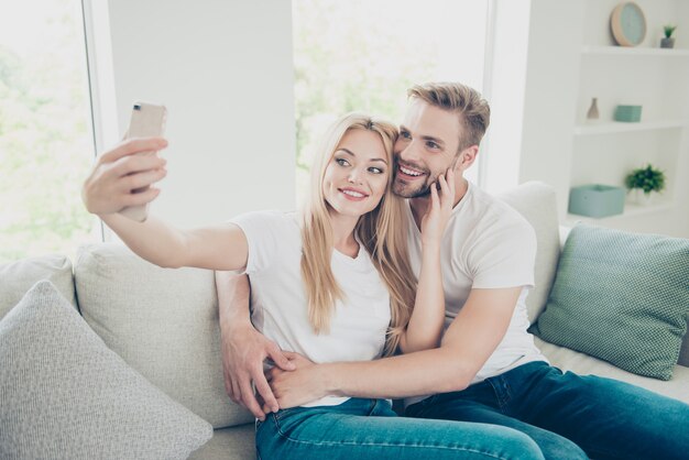 Beau couple élégant en t-shirts et jeans décontractés à la maison faisant selfie