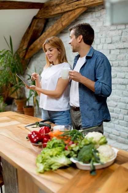 Beau couple gai, cuisiner ensemble, dînant à la recherche d&#39;une tablette numérique et s&#39;amuser dans la cuisine rustique