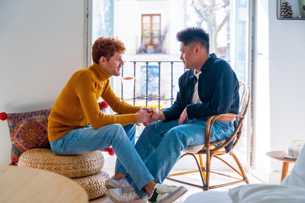 Beau couple gay étant romantique à la maison près du balcon à la maison parler et serrer la main concept lgbt