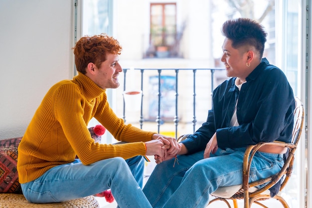 Beau couple gay étant romantique à la maison près du balcon à la maison parler et serrer la main concept lgbt