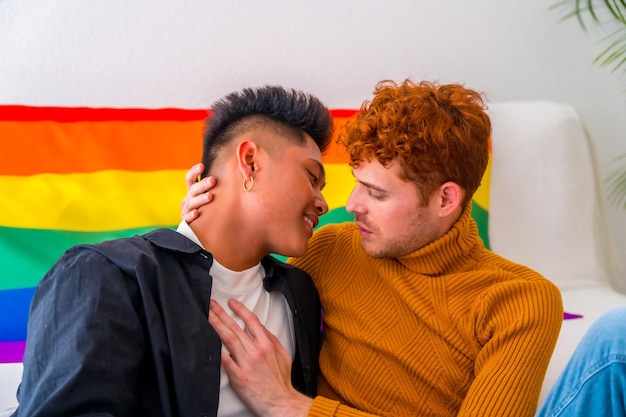 Beau couple gay étant romantique à la maison près du canapé embrassant le drapeau arc-en-ciel du concept lgbt