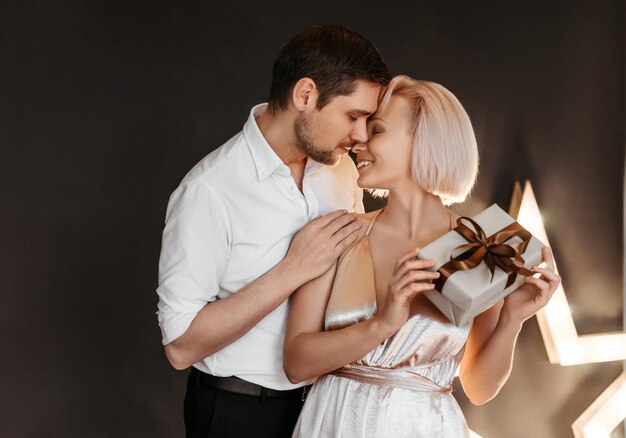 Beau couple heureux jeune famille en robes de soirée jeune femme avec boîte-cadeau sur fond sombre