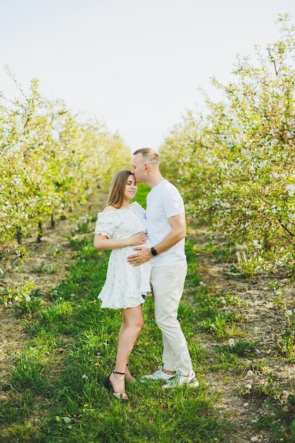 Un beau couple de jeunes hommes et femmes enceintes dans le jardin de printemps un concept de famille de style de vie de beauté une mère heureuse attend un bébé un jeune couple heureux dans un jardin en fleurs