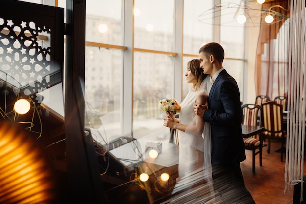 Beau couple de jeunes mariés regarde par la fenêtre dans un intérieur moderne, effet flare, double exposition.