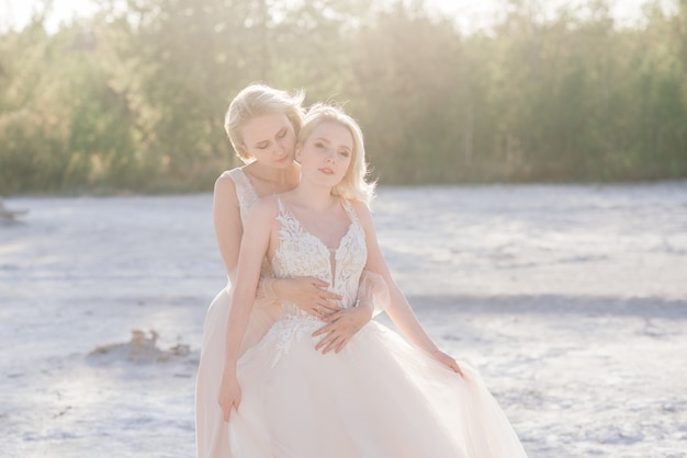 Beau couple de lesbiennes marchant sur le sable le long de la rivière le jour de leur mariage