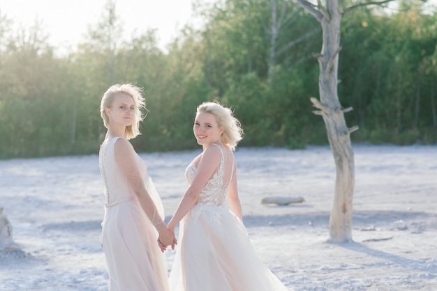 Beau couple de lesbiennes marchant sur le sable le long de la rivière le jour de leur mariage