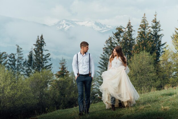 Beau couple de mariage, mariée et marié, amoureux sur fond de montagnes. Le marié dans un beau costume et la mariée dans une robe de luxe blanche. Le couple de mariés marche.