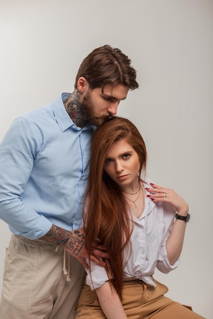 Beau couple à la mode élégant bel homme brutal avec un tatouage et une barbe et une belle fille modèle rousse dans une chemise blanche