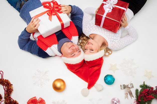 Beau couple de Noël en chapeaux de père Noël couché avec des cadeaux sur fond blanc