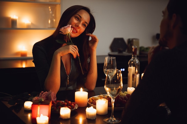 Beau couple passionné ayant un dîner romantique aux chandelles à la maison, femme sentant une fleur