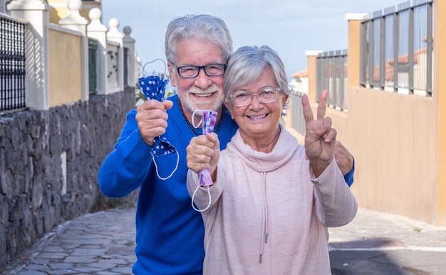 Beau couple de personnes âgées déjà vacciné contre l'infection à coronavirus - sourit joyeusement à l'extérieur en enlevant ses masques de protection