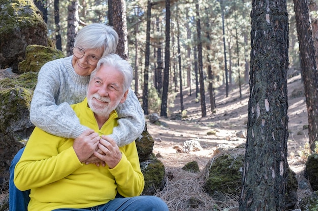 Beau couple de personnes âgées heureux assis dans la forêt, main dans la main Femme caucasienne embrassant son mari souriant Personnes âgées aux cheveux gris profitant de la liberté de vacances et de la randonnée dans la nature par une journée ensoleillée