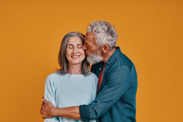 beau couple de personnes âgées s'embrassant et souriant tout en se tenant ensemble sur fond orange