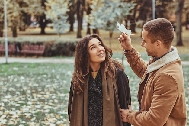 Beau couple profite d'une promenade d'une journée au parc d'automne, l'homme tient une feuille d'érable.