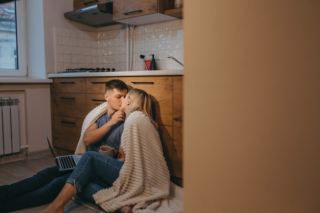 Beau couple recouvert d'une couette s'embrassent dans la cuisine sur le sol