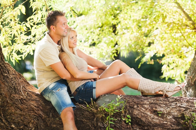 Beau couple romantique embrassé dans le parc assis sur l'arbre.