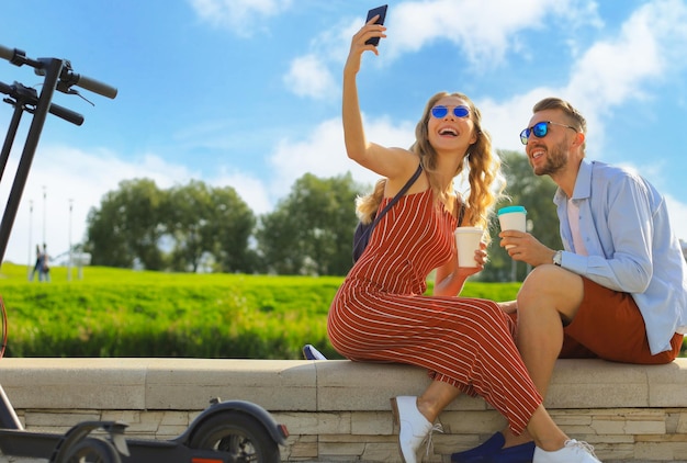 Beau couple s'amusant à conduire un scooter électrique à travers la ville en faisant une pause en prenant un selfie