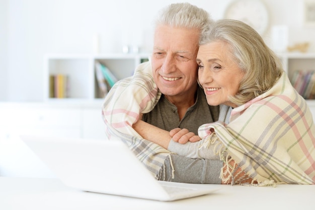 Beau couple senior avec couverture à l'aide d'un ordinateur portable à la maison