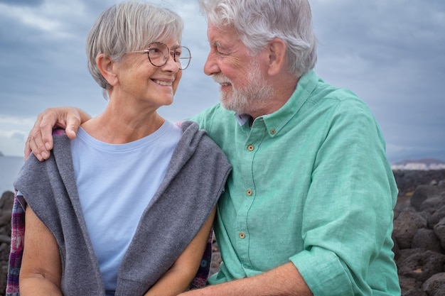 Beau couple senior heureux assis ensemble sur la falaise se regardant dans les yeux Joyeux homme et femme aux cheveux blancs âgés profitant de vacances ou de retraite