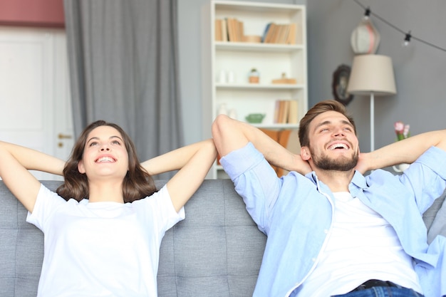 Beau couple souriant assis sur un canapé et rêvant d'une nouvelle maison.