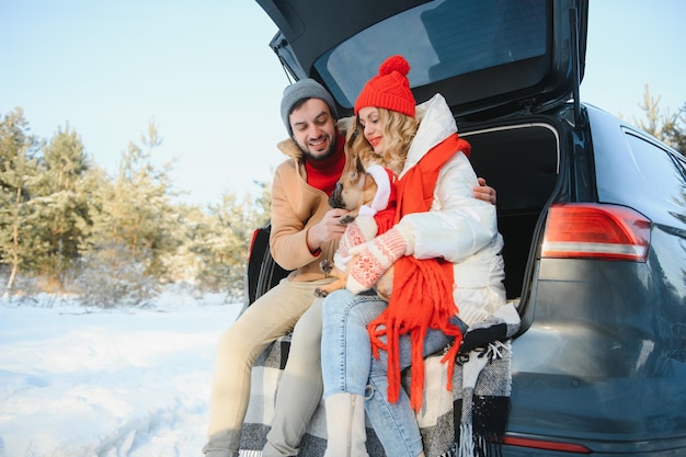 Beau couple souriant assis dans le coffre de la voiture dans la forêt d'hiver