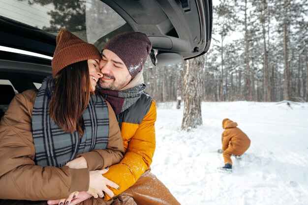 Beau couple souriant assis dans le coffre de la voiture dans la forêt d'hiver