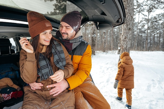 Beau couple souriant assis dans le coffre de la voiture dans la forêt d'hiver