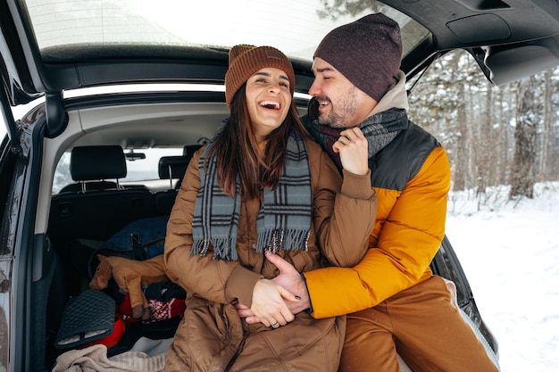Un beau couple souriant assis dans le coffre d'une voiture dans la forêt d'hiver