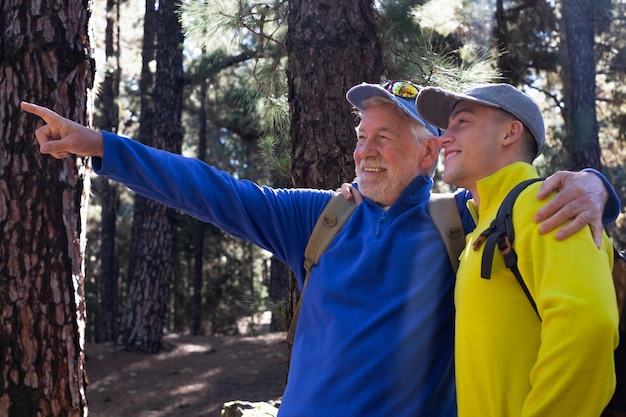 Photo beau couple souriant et insouciant de grand-père et de jeune petit-fils marchant dans les montagnes partageant la même passion pour la nature et un mode de vie sain ensemble dans les bois l'aventure n'a pas d'âge