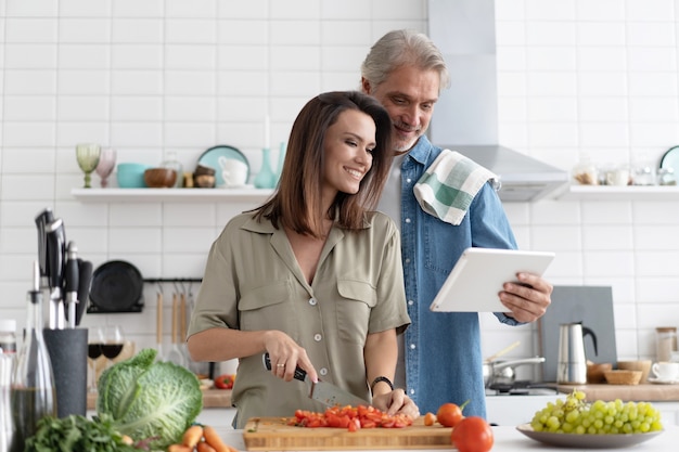 Beau couple utilisant une tablette numérique et souriant tout en cuisinant dans la cuisine à la maison