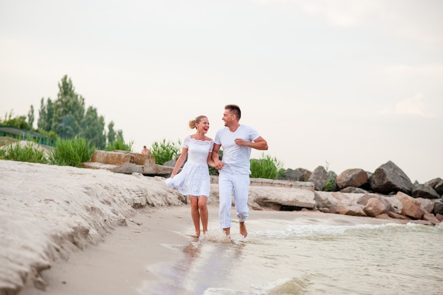 Beau couple en vêtements blancs marchant sur la mer