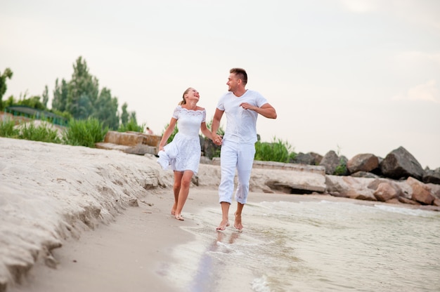 Beau couple en vêtements blancs marchant sur la mer