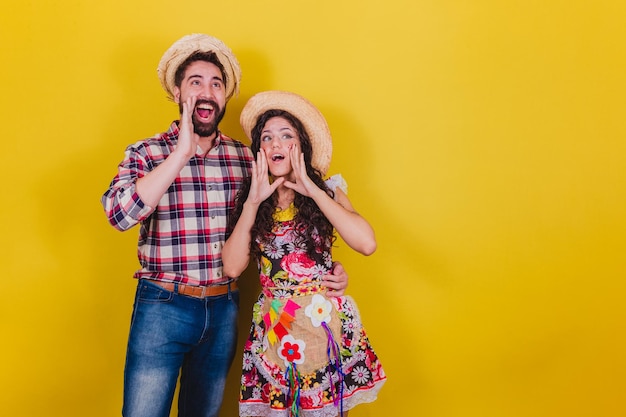 Beau couple vêtu de vêtements typiques pour une Festa Junina Arraia de Sao Joao appelant et criant bruyamment promotion