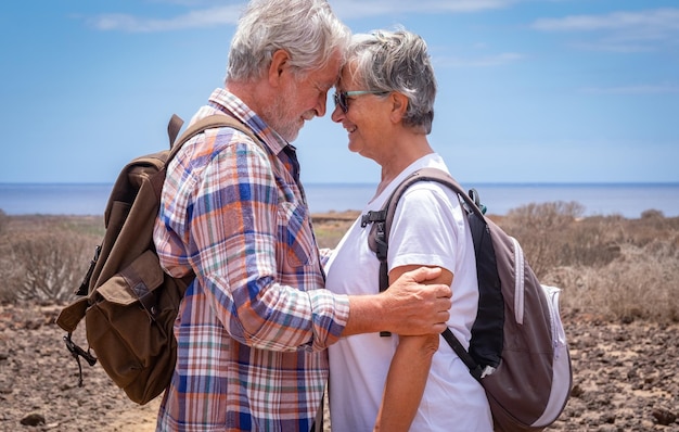 Beau couple de voyageurs seniors en excursion en plein air dans un paysage aride portant un sac à dos et souriant Horizon sur la mer