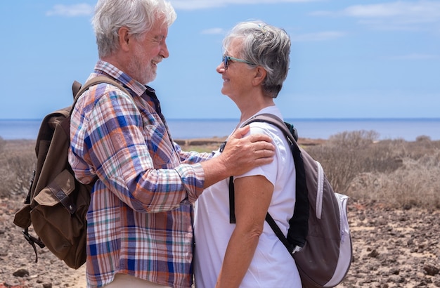 Beau couple de voyageurs seniors avec sac à dos regardant dans les yeux en excursion en plein air. Horizon sur la mer