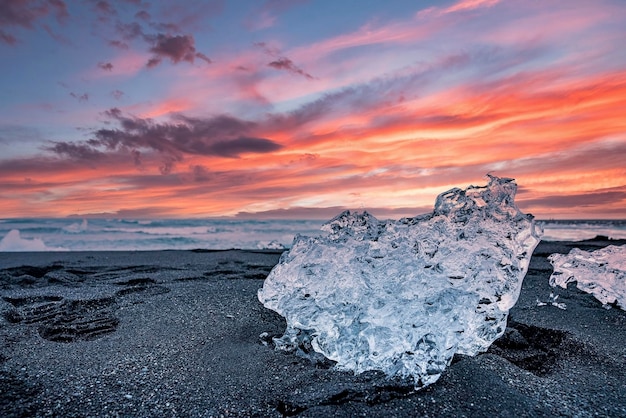 Beau cristal de glace sur le sable noir de la plage de diamant contre le ciel nuageux au coucher du soleil