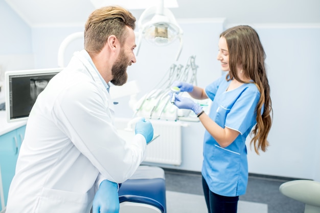 Beau dentiste avec une jeune assistante en uniforme se préparant au travail au cabinet dentaire