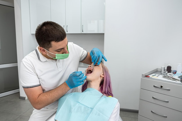 Un beau dentiste masculin effectue un traitement pour une jeune patiente qui aide la dentisterie au traitement