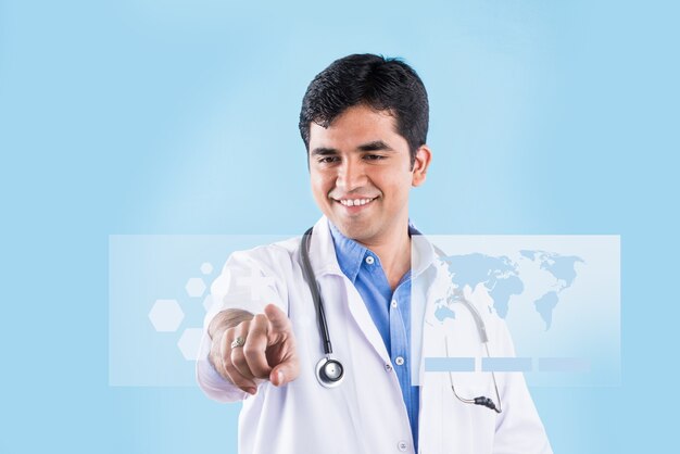 Beau docteur indien touchant l'écran virtuel avec l'index. debout isolé sur fond bleu