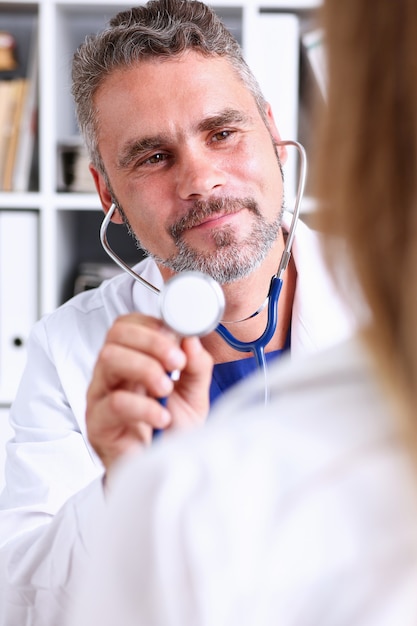 Beau docteur mature tenir dans la tête de stéthoscope de bras