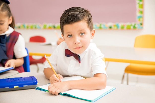 Beau enfant d'âge préscolaire latin en uniforme prêtant attention à la classe et travaillant sur un devoir d'écriture à l'école