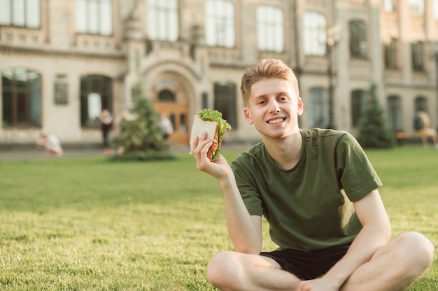 Beau étudiant universitaire mangeant un sandwich appétissant