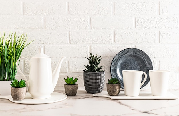 Beau fond de cuisine aux couleurs claires avec une cafetière blanche et deux tasses sur un comptoir en marbre avec des fleurs d'intérieur en pot