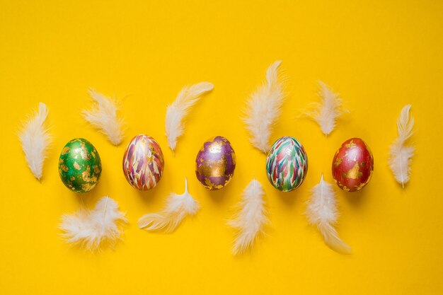 Beau fond d'écran coloré de Pâques, bannière avec des oeufs de Pâques peints et des plumes blanches sur fond jaune.