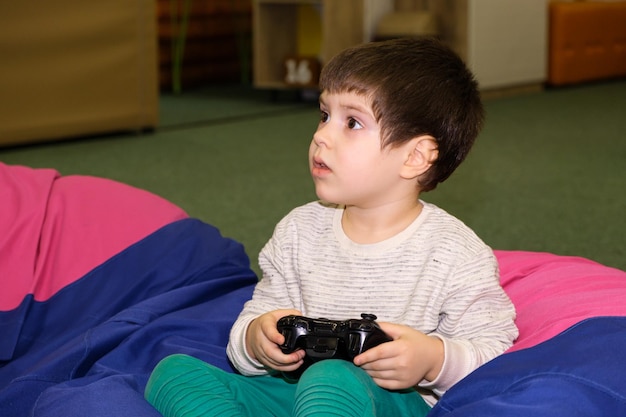 Un beau garçon de 4 ans joue sur une console de jeu tient un joystick dans ses mains et regarde au loin une place pour le texte