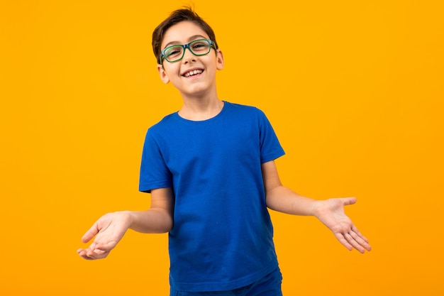 Beau garçon adolescent dans un t-shirt bleu avec des lunettes posant sur un fond jaune avec copie espace