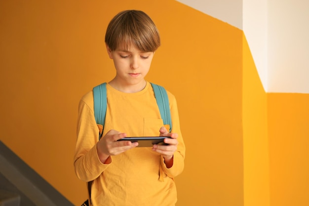 Un beau garçon adolescent dans un t-shirt jaune debout et discutant au téléphone près d'un mur jaune