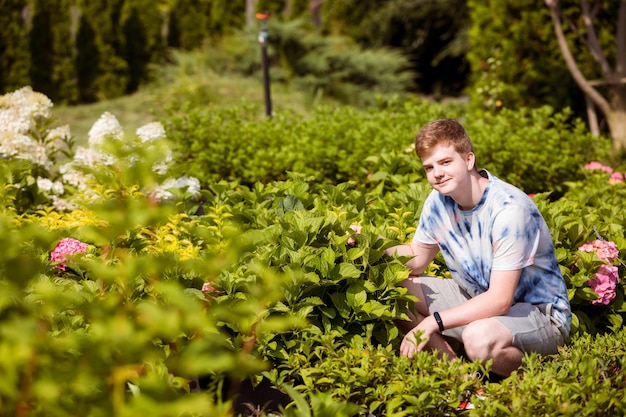 Beau garçon adolescent avec un grand pot de fleur d'hortensia pendant un travail d'été à temps partiel sur le marché des plantes en plein air