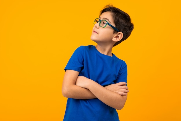 Beau garçon adolescent vêtu d'un T-shirt bleu et des verres se tient avec les bras croisés sur jaune avec copie espace